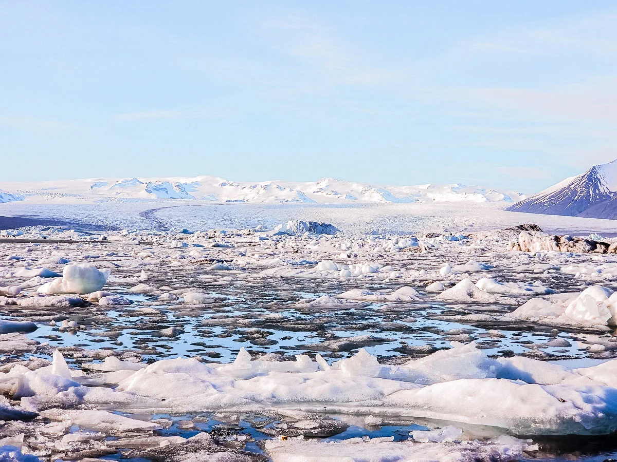 A remote and icy landscape on a sunny day in Iceland. There are snow capped mountains in the distance.