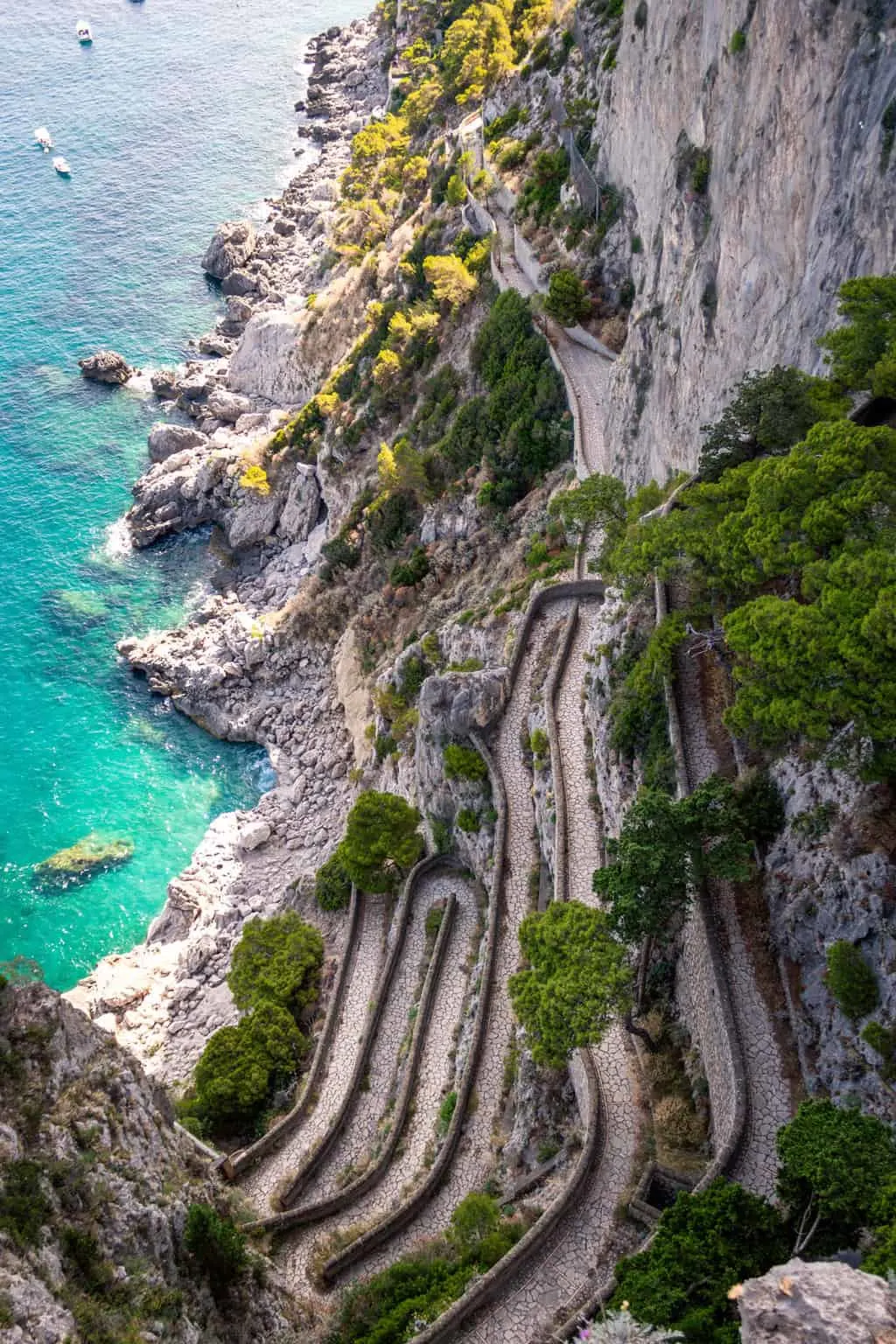 Looking down at a tightly winding road on the coast of clear water.