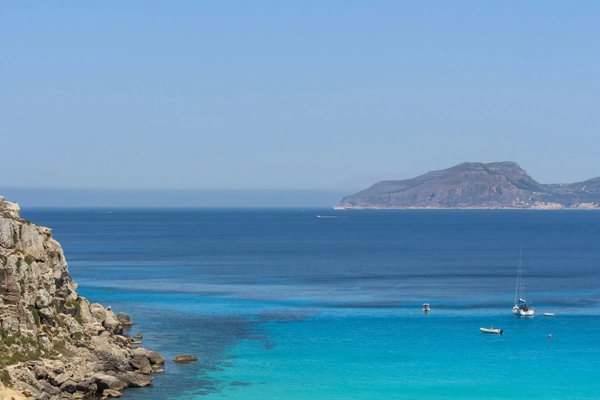 Boats moored in clear blue water wurrounded by rocky islands on a sunny day. 