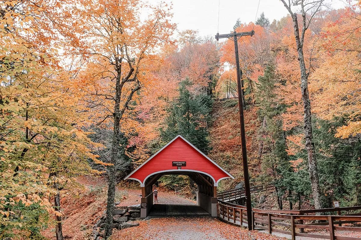 Red wooden covered bridge surrounded by fall foliage in New Hampshire.