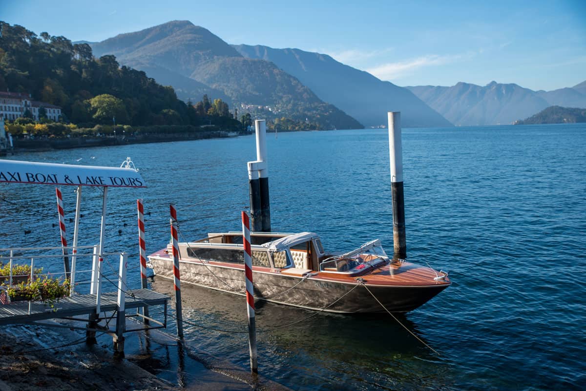 A polished woden taxi boat tied up to red and white stripe poles on Lake Como. 
