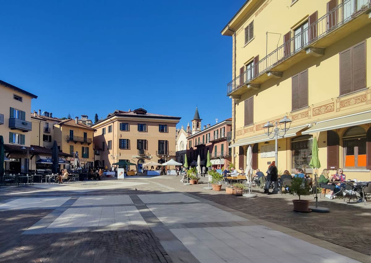 people sitting at outdoor cafes in a traditional Italian plaza surrounded by yellow buildings. 