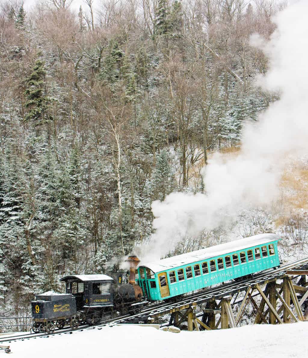 The traitional steam cog train with a green carriage makes its way dow the snowy mountain.