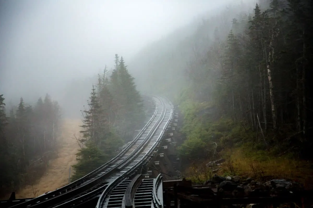 The Mt. Washington Cog Railway is surrounded by wooded forest on a cold, windy, foggy morning in the White Mountains National Forest.
