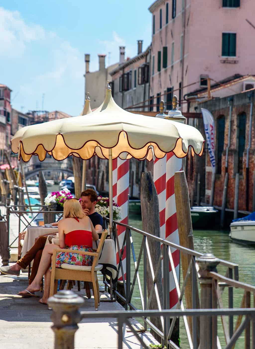A young couple sit under an umbrella at a waterfront cafe in Venice in summer. 