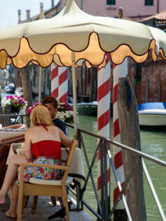 A young couple sit under an umbrella at a waterfront cafe in Venice in summer.