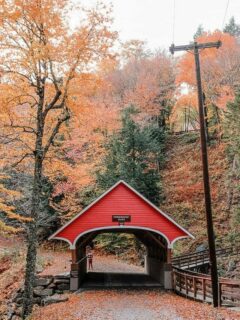 Red wooden covered bridge surrounded by fall foliage in New Hampshire.
