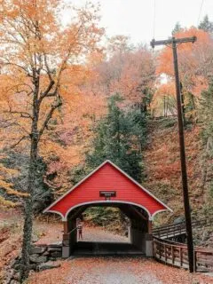 Red wooden covered bridge surrounded by fall foliage in New Hampshire.