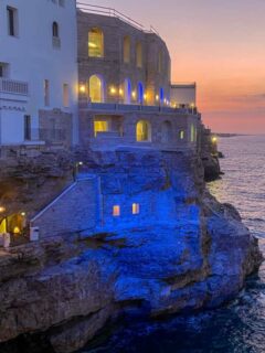 An Italian city built into the rocks overlooking the ocean at night. people are dining at a restaurants in the rock face.