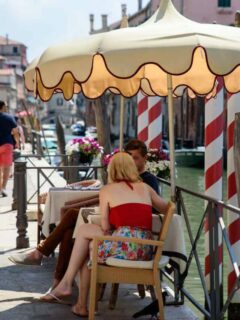 A young couple sit under an umbrella at a waterfront cafe in Venice in summer.