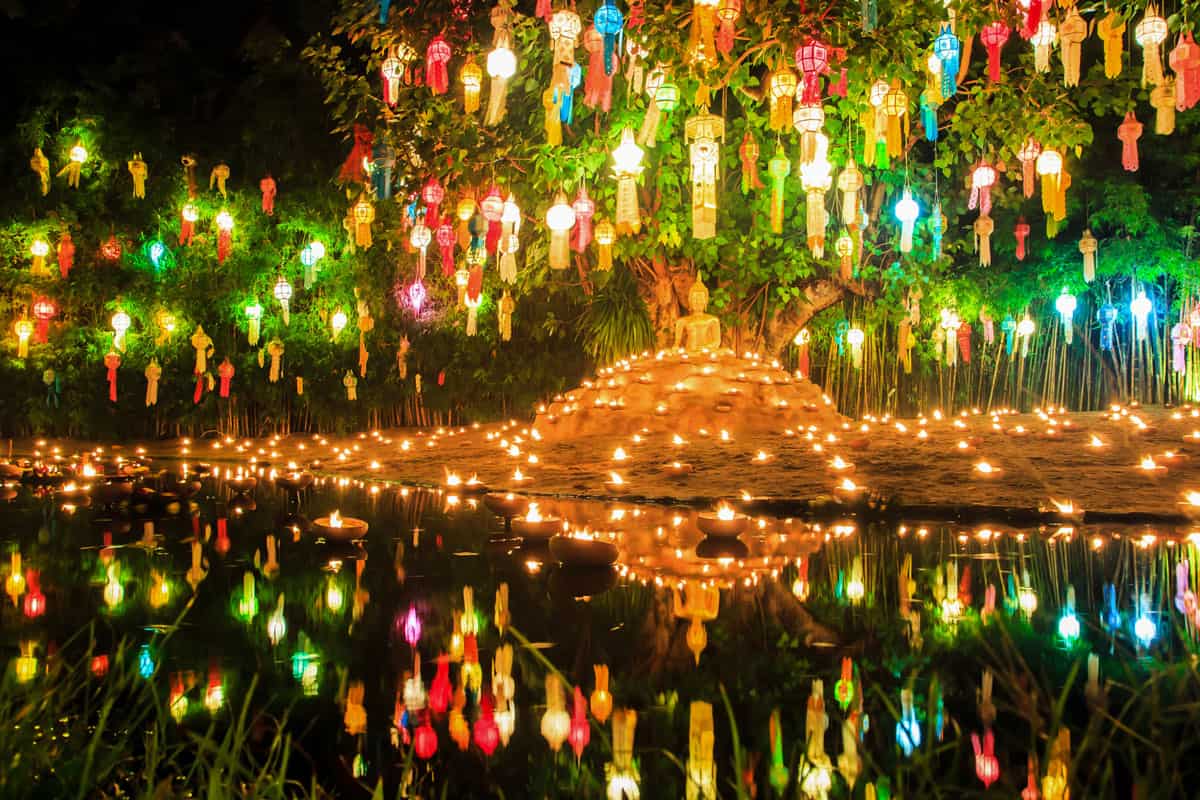 Lanterns hang over a buddha statu in Chiang Mai at night reflecting in the water. 