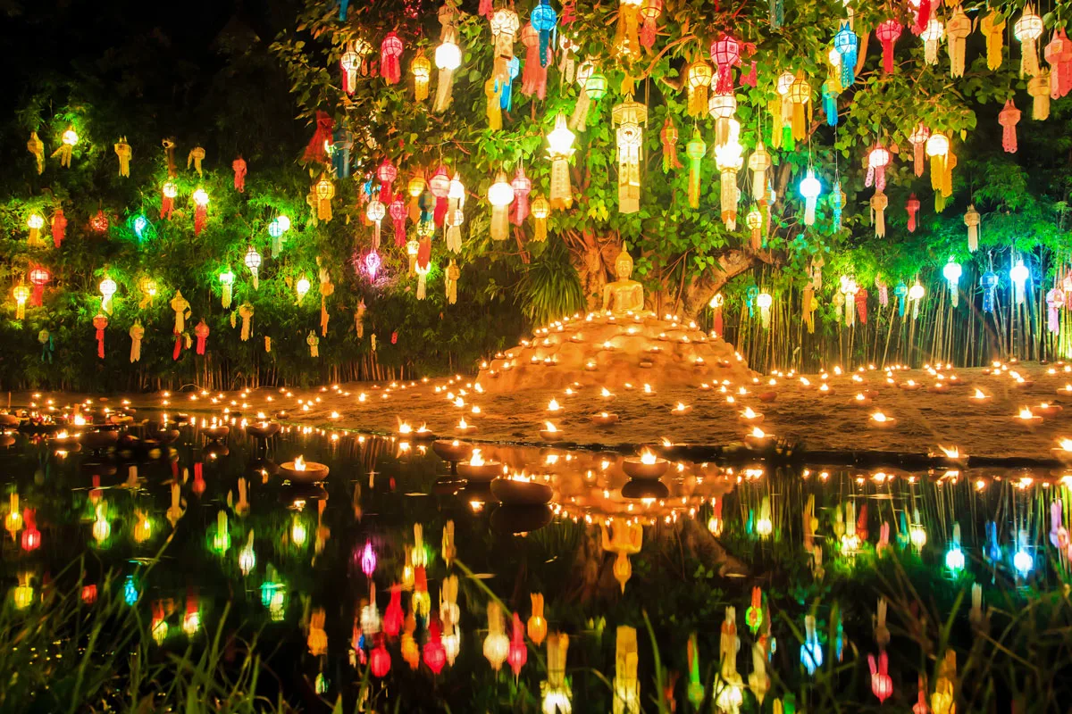 Lanterns hang over a buddha statu in Chiang Mai at night reflecting in the water. 