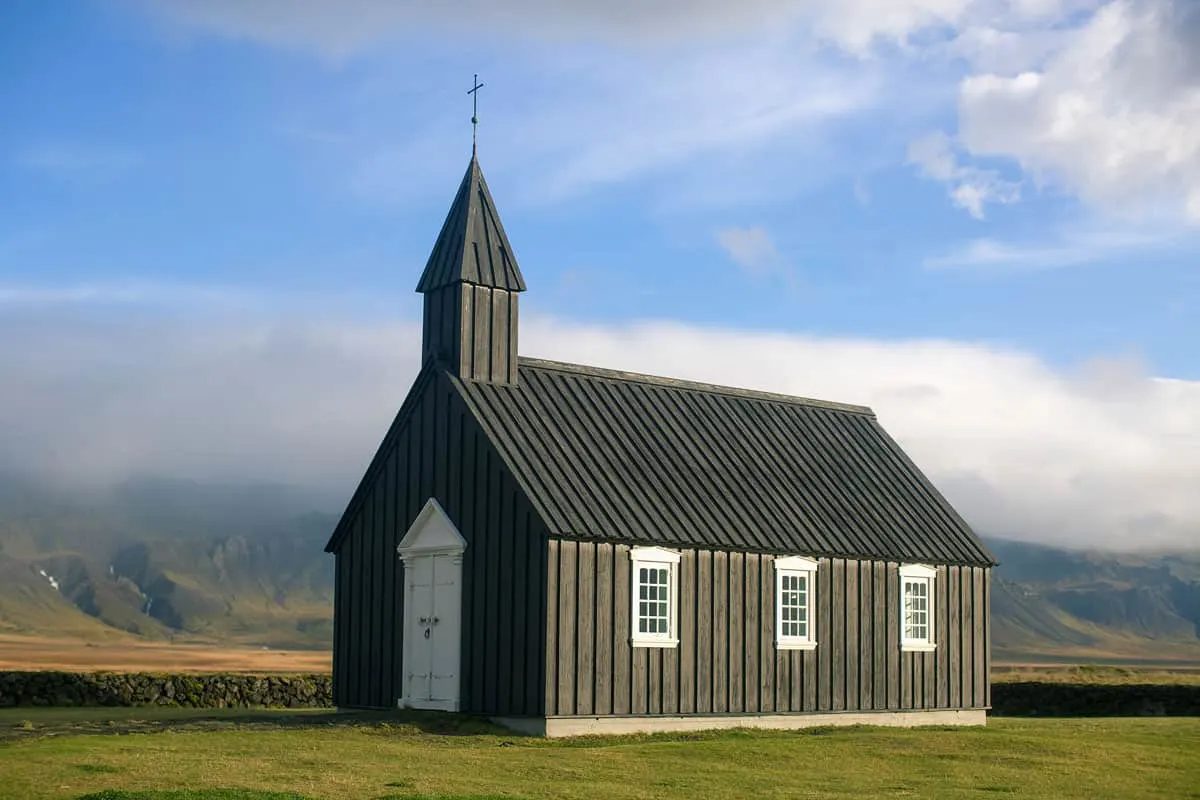Black wooden church on a flat field in Iceland.