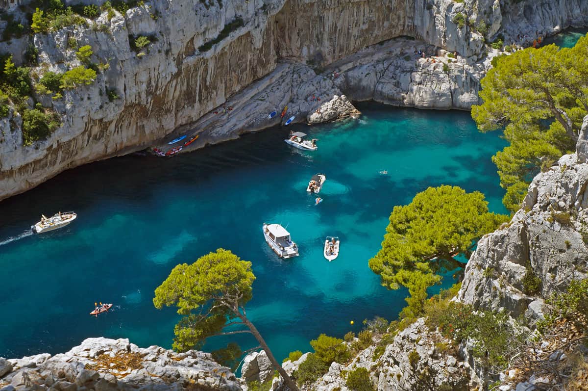 Boats and kayaks in the clear blue water in between white cliffs in the Calanques National Park.