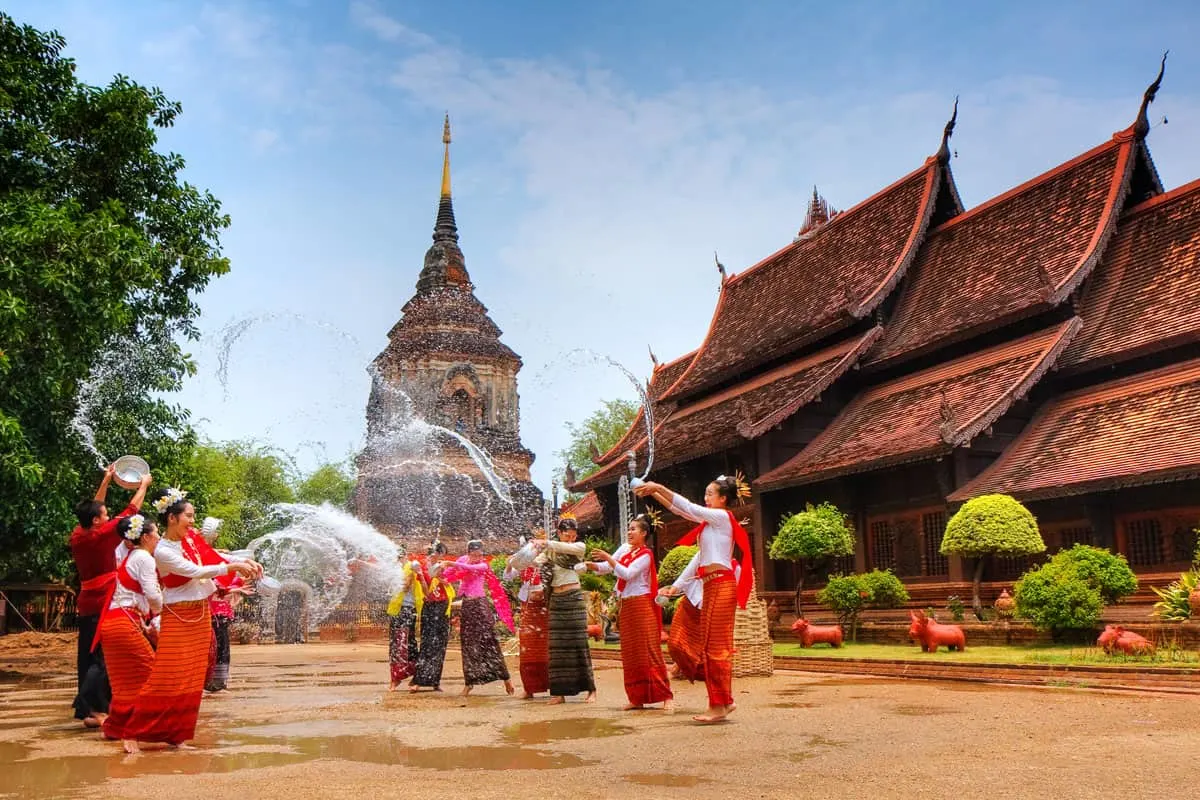 Thai ladies in traditiona dress throwing waterat each other in front of Buddhist temples on Songkran festival.  