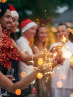 Group of friends with champange wearing Christmas hats holding sparklers.