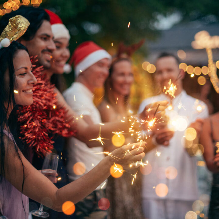 Group of friends with champange wearing Christmas hats holding sparklers.