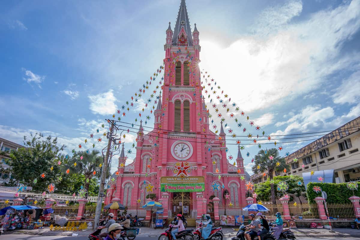 Bright pink gothic church in Vietnam with scooter traffic driving past.