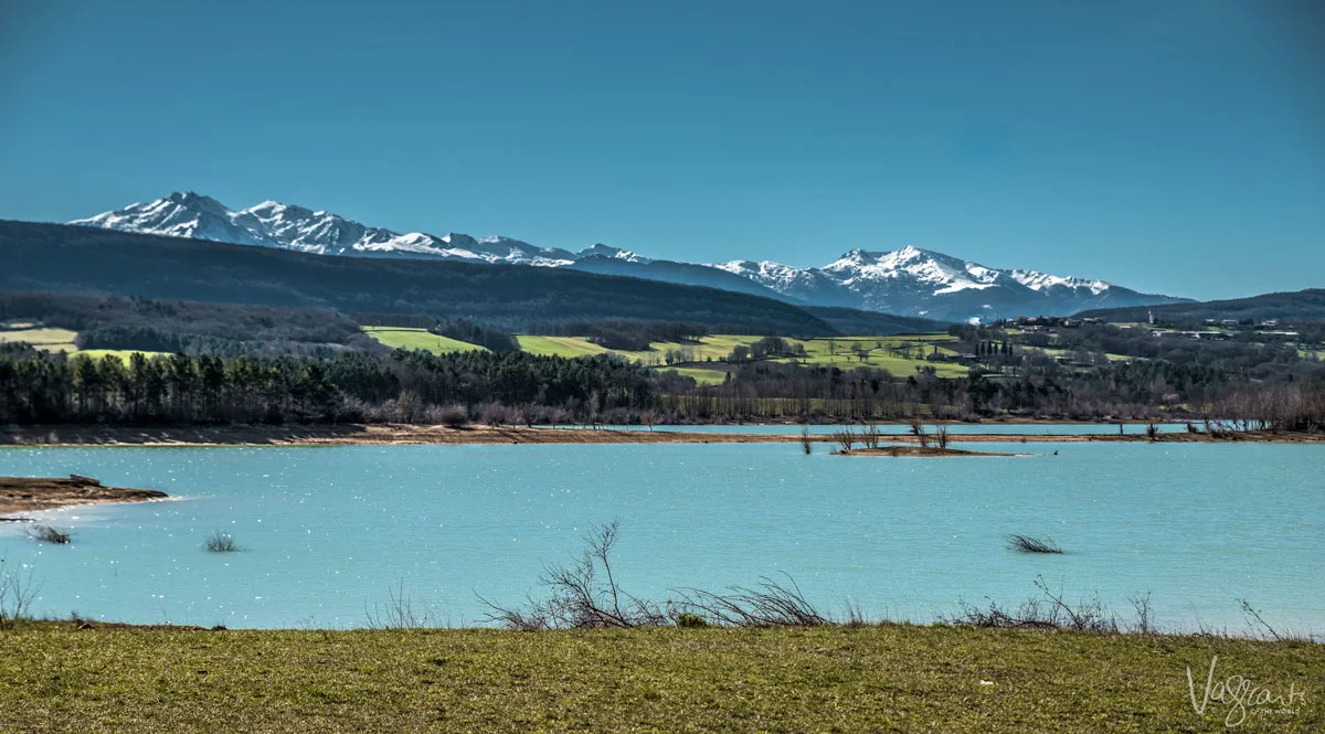 A bright blue lake with snow capped mountains in the distance.