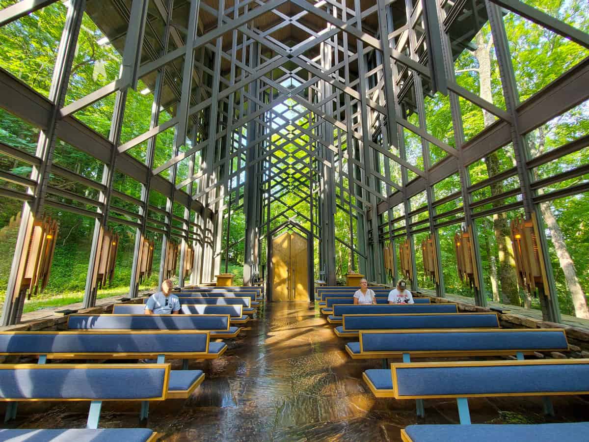 people sitting in a glass church surrounded by green forest.