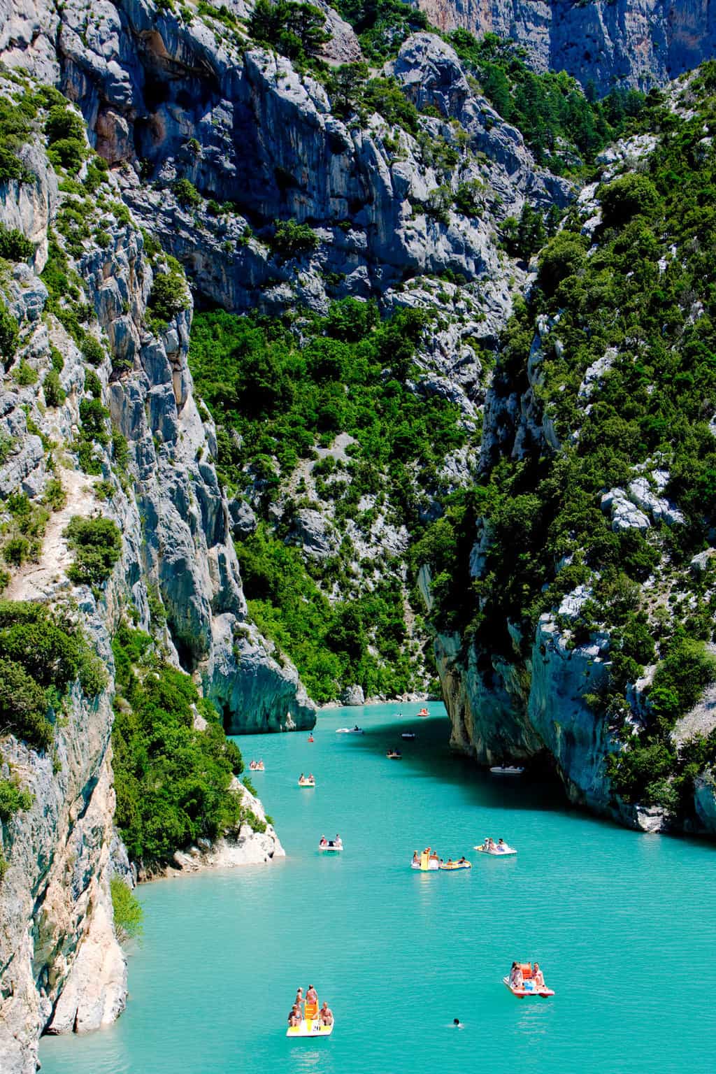 people on paddle boats on turquoise blue water surrounded by white limestone cliffs. 