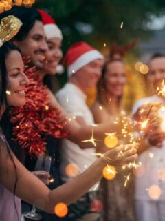 Group of friends with champange wearing Christmas hats holding sparklers.