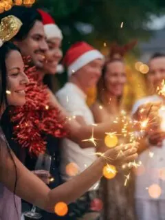 Group of friends with champange wearing Christmas hats holding sparklers.