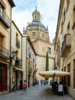 Narrpw street in Salamanca with domed cathedral at the end.