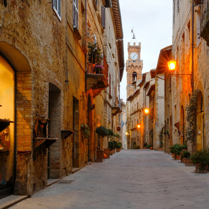 Ancient street in Pienza with stone buildings dimly lit, in the background the city hall bell tower.