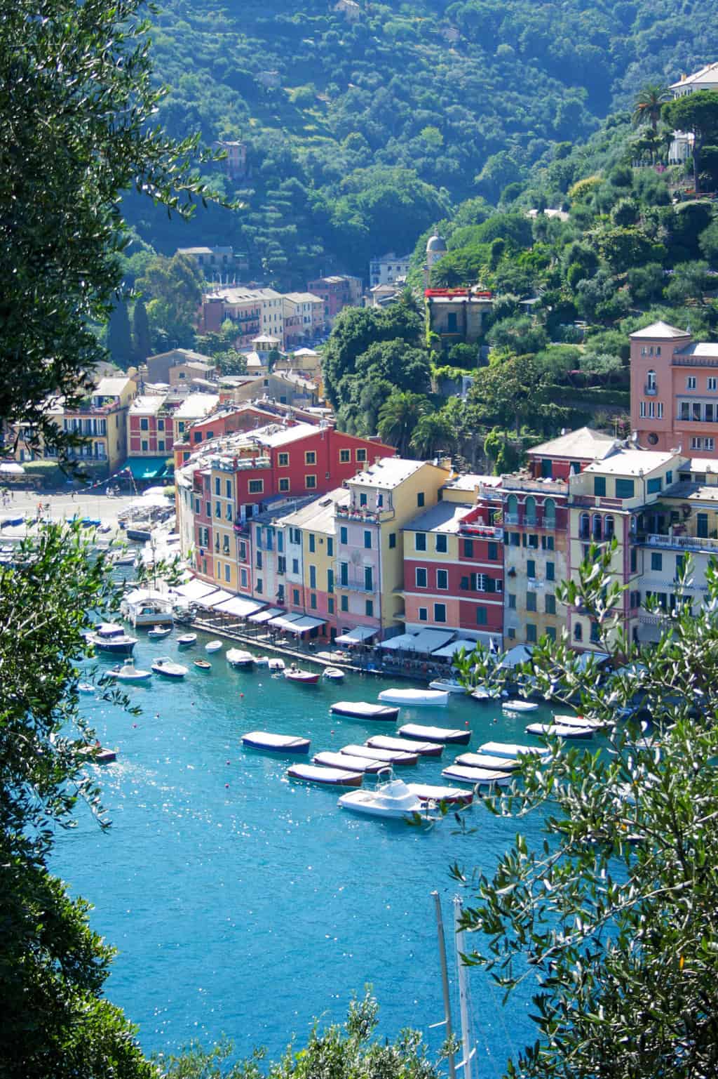 Small boats moored on clear blue water in front of the colourful village of Portofino.