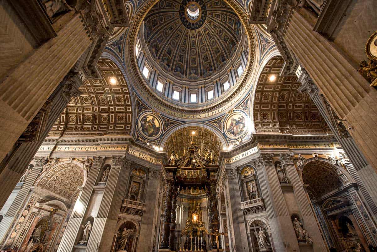 Inside St Peter's Basilica in the Vatican looking up at the ornate dome covered with frescoes and gilded decoration.