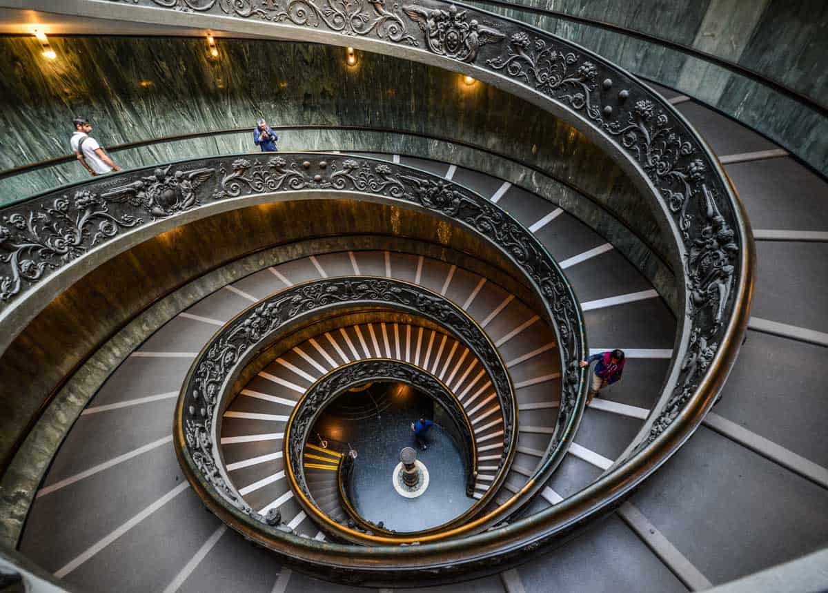 People walk down the black and grey spiral staircase in the Vatican Museum.