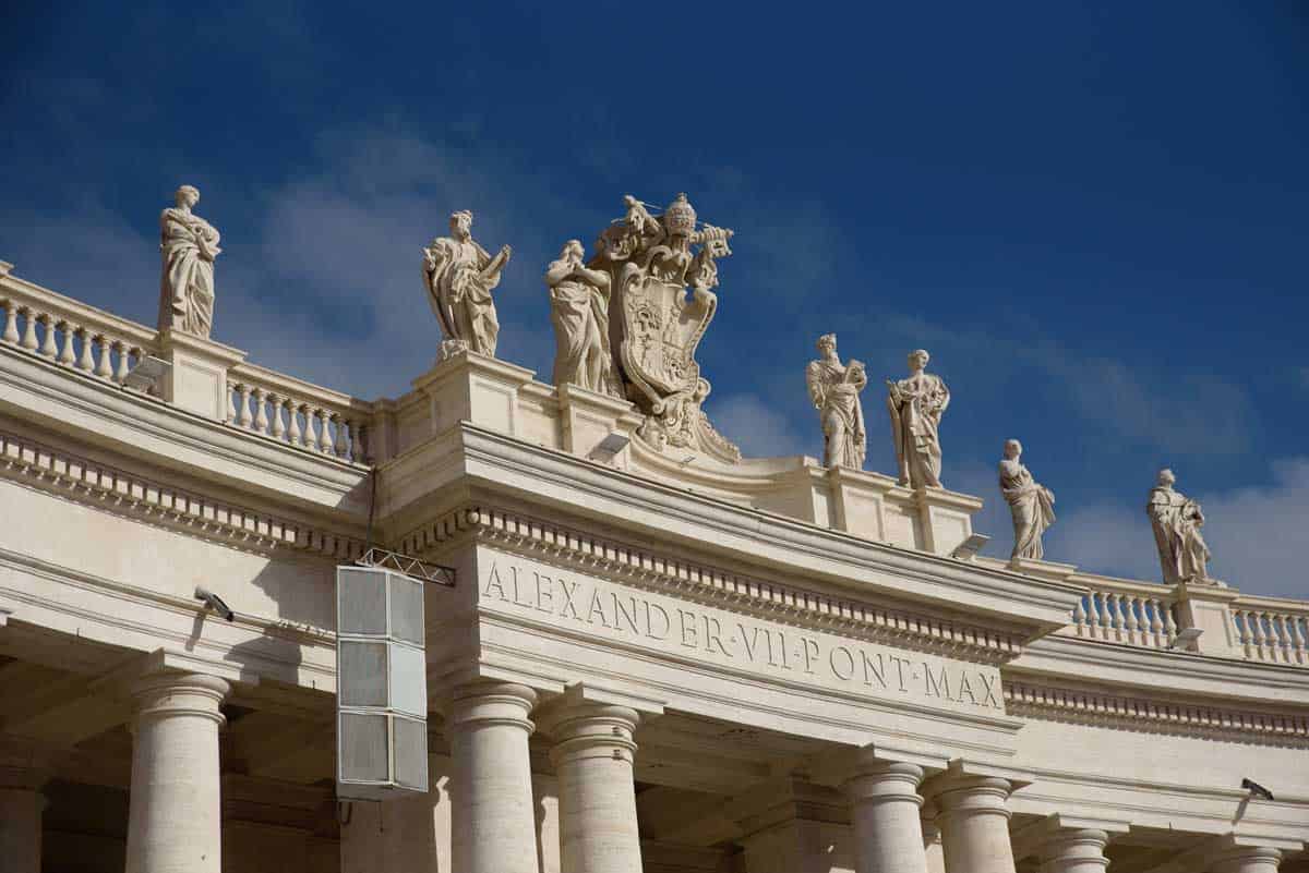 A line of statues on a roof against a blue sky in the Vatican.