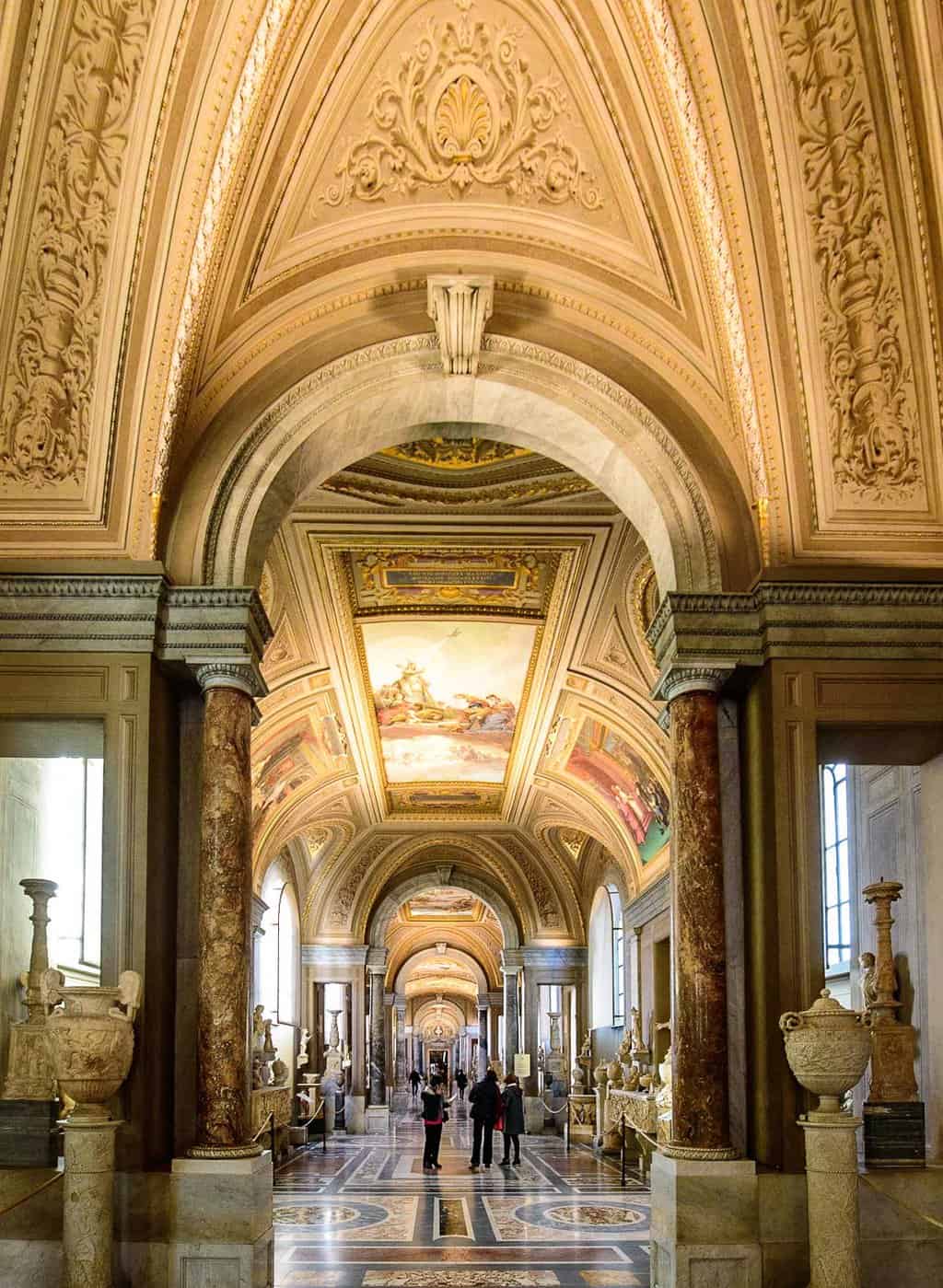 People walking down the ornate halls of the Vatican Museums.