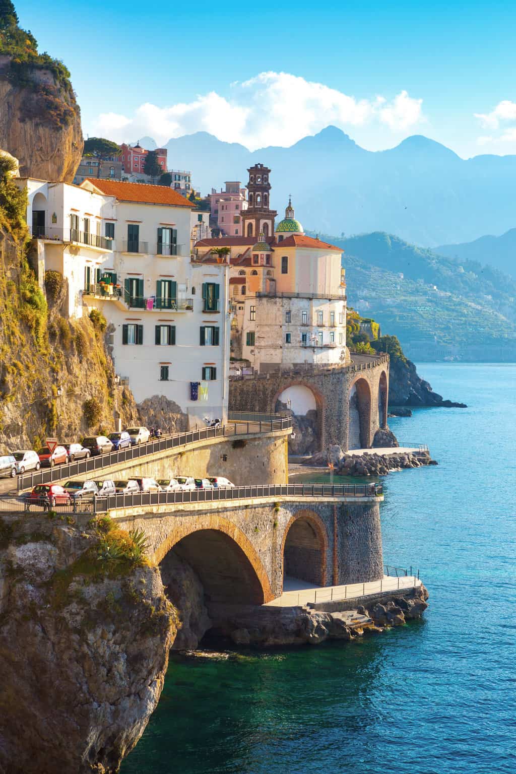 A costal town on the cliffs of the Amalfi coast overlooking the water with hills in the soft orange glow of morning.