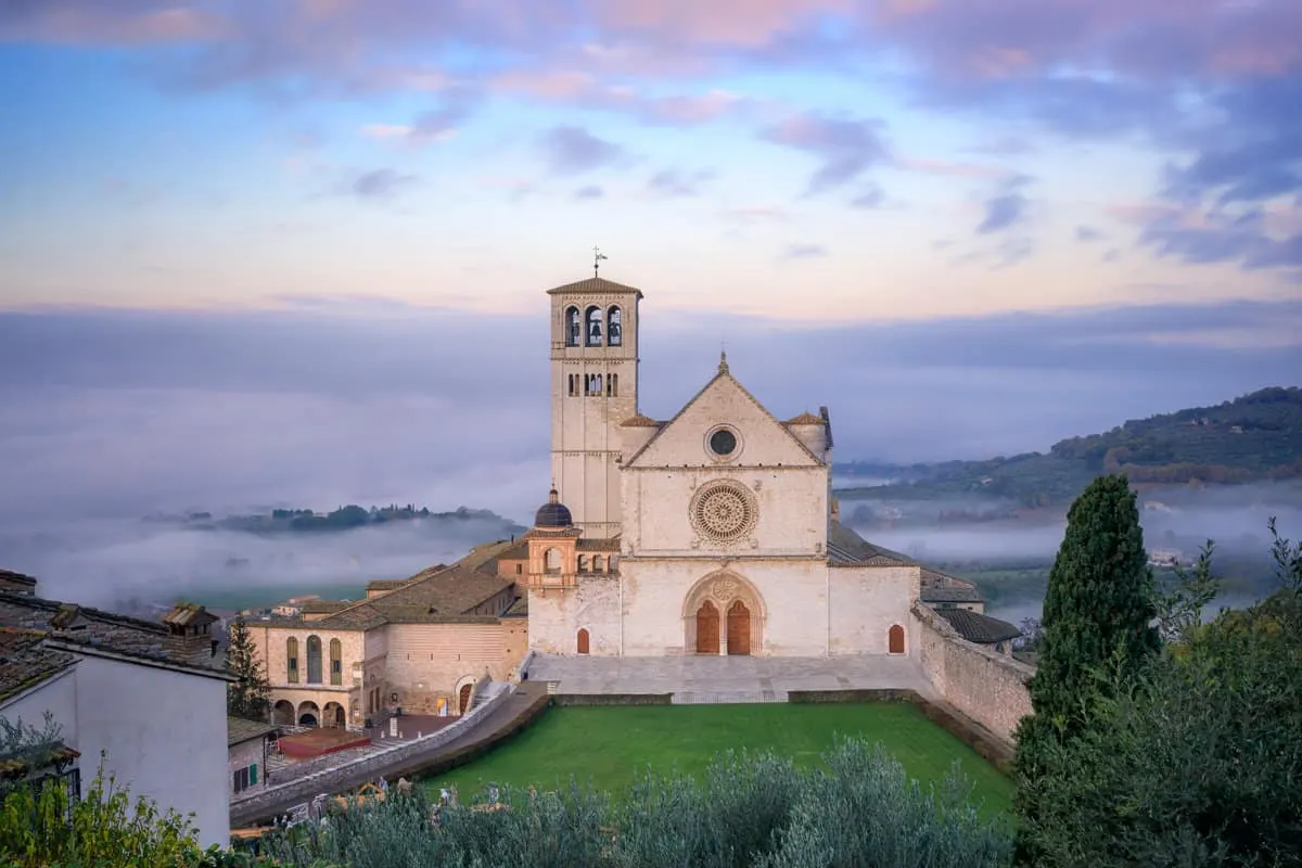 The Basilica of San Francesco in Assisi in the morning light surrounded by fog.