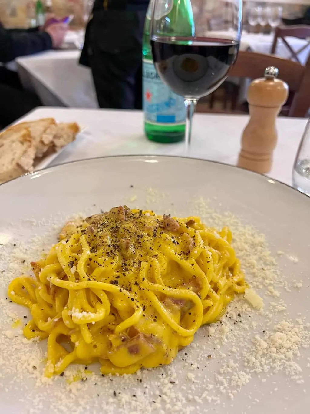 A plate of traditional carbonara pasta with a glass of red wine in a restaurant in Rome.