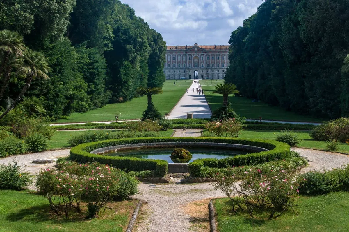 Ornate landscaped gardens with long, tall hedges lead to a palace in the distance.