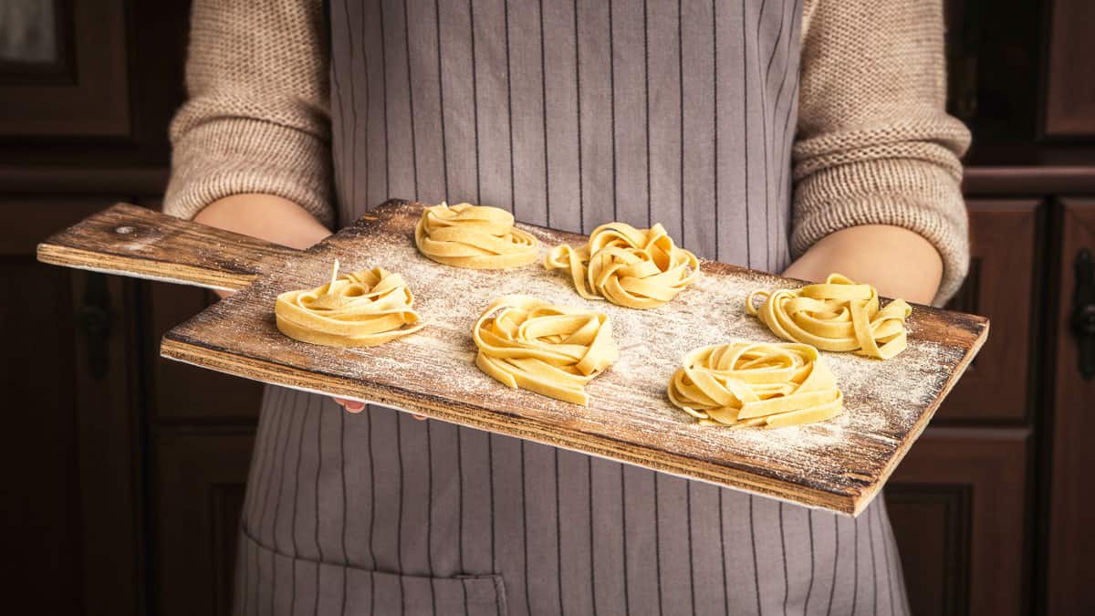 Woman chef holding wooden board with fettuccine nests