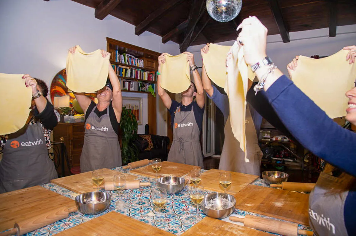A group of people hold up sheets of pasta dough at an Italian cooking class.
