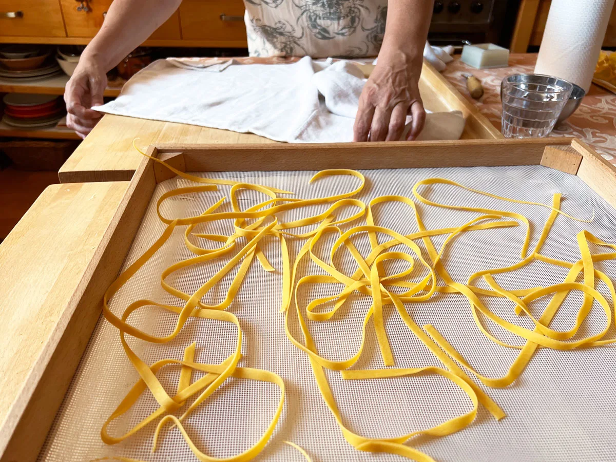 A womans hands on a floury board with a rack of fresh made fettuccini at a pasting making class in Rome.  
