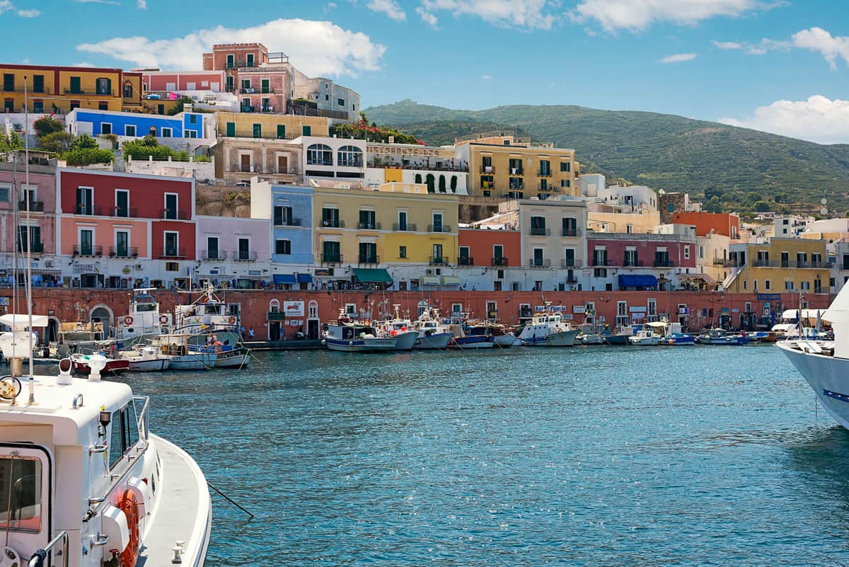 Colourful buildings line the waterfront with boats moored in the harbour ona sunny day on Ponza Island in Italy.