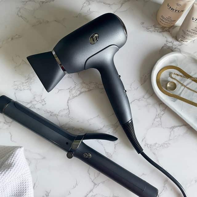 Black travel hairdryer on a marble counter with a hair straightener. 