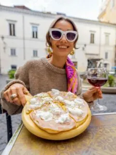 A glamorous woman in sunglasses eating Pizza at an outdoor Italian restaurant in Rome.