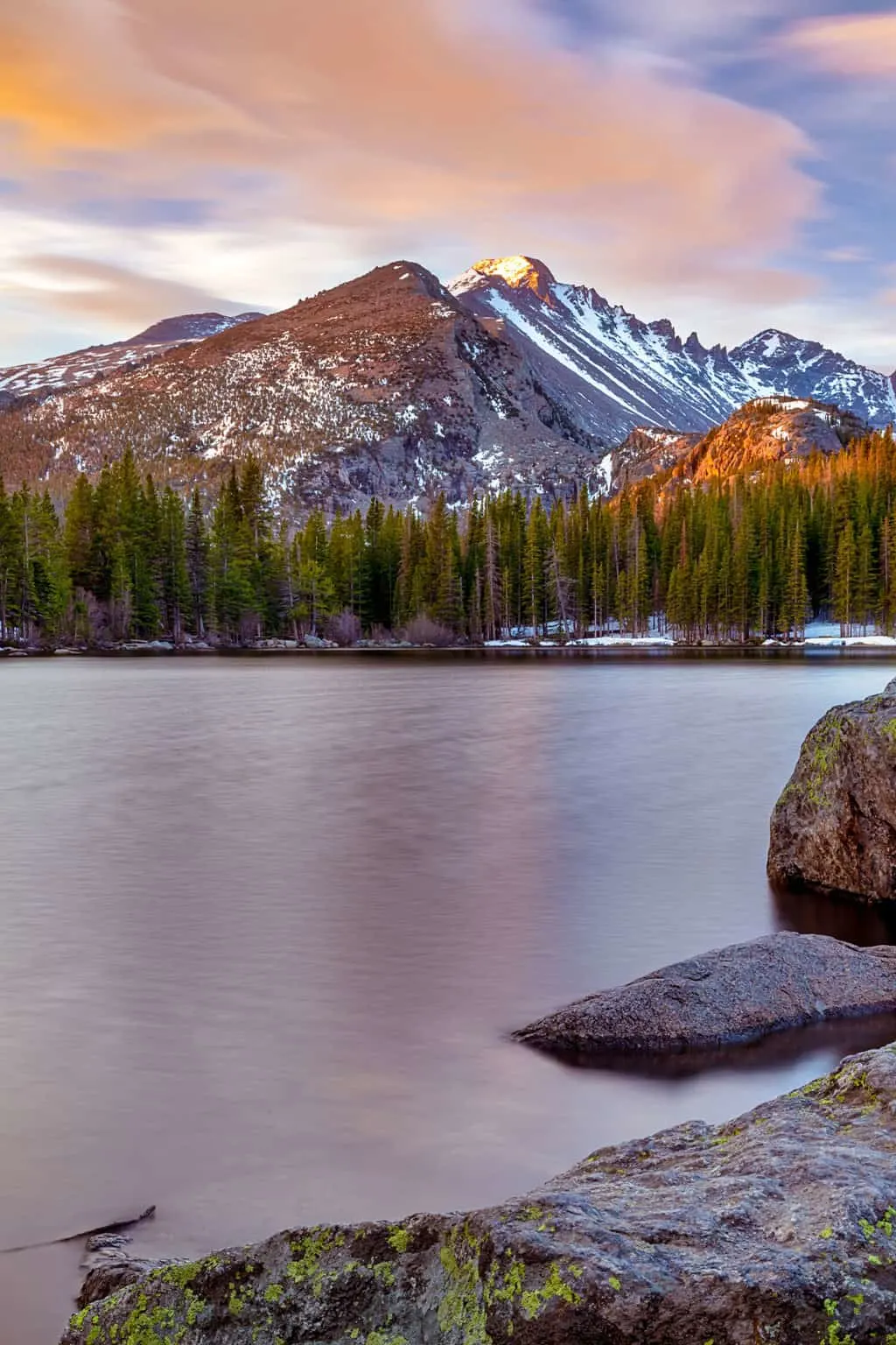 Snow capped mountains on the other side of a still lake. Dusk created a purple glow over the landscape.
