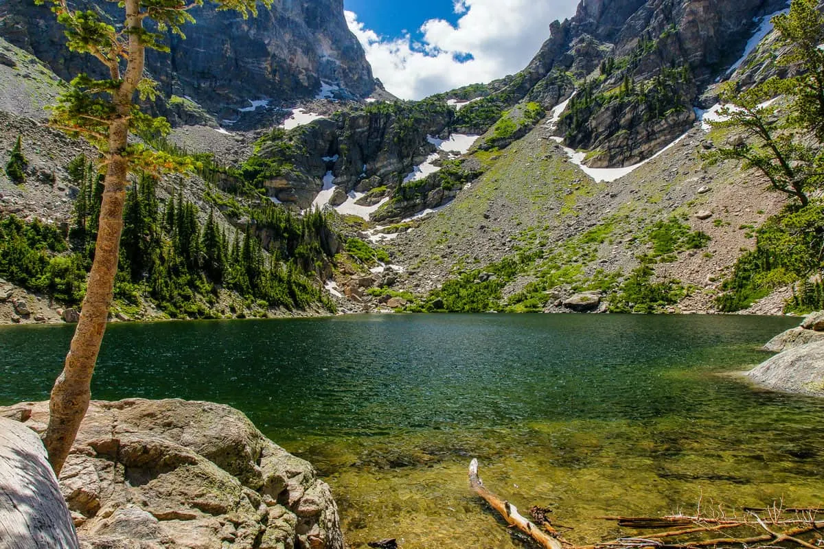 An emerald green lake surrounded by green mountainous hill dusted with snow.