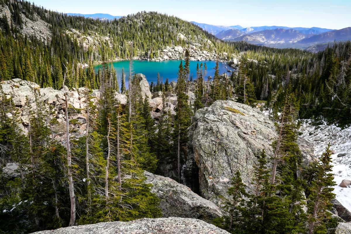 A vivid blue lak in the center of cracky mountain peaks covered with sparse wooded forests.