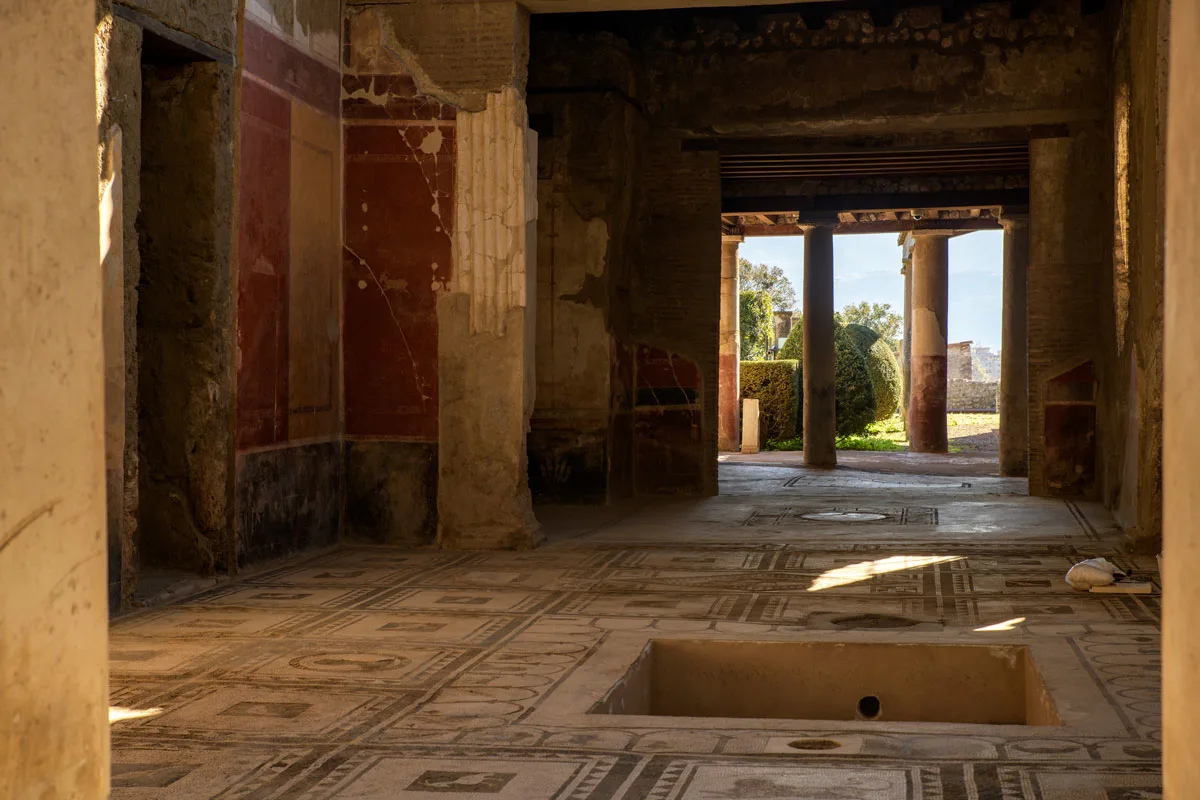 Inside an ancient oman house in Pompeii with mosaic floors and view to a landscaped garden at the back of the house.