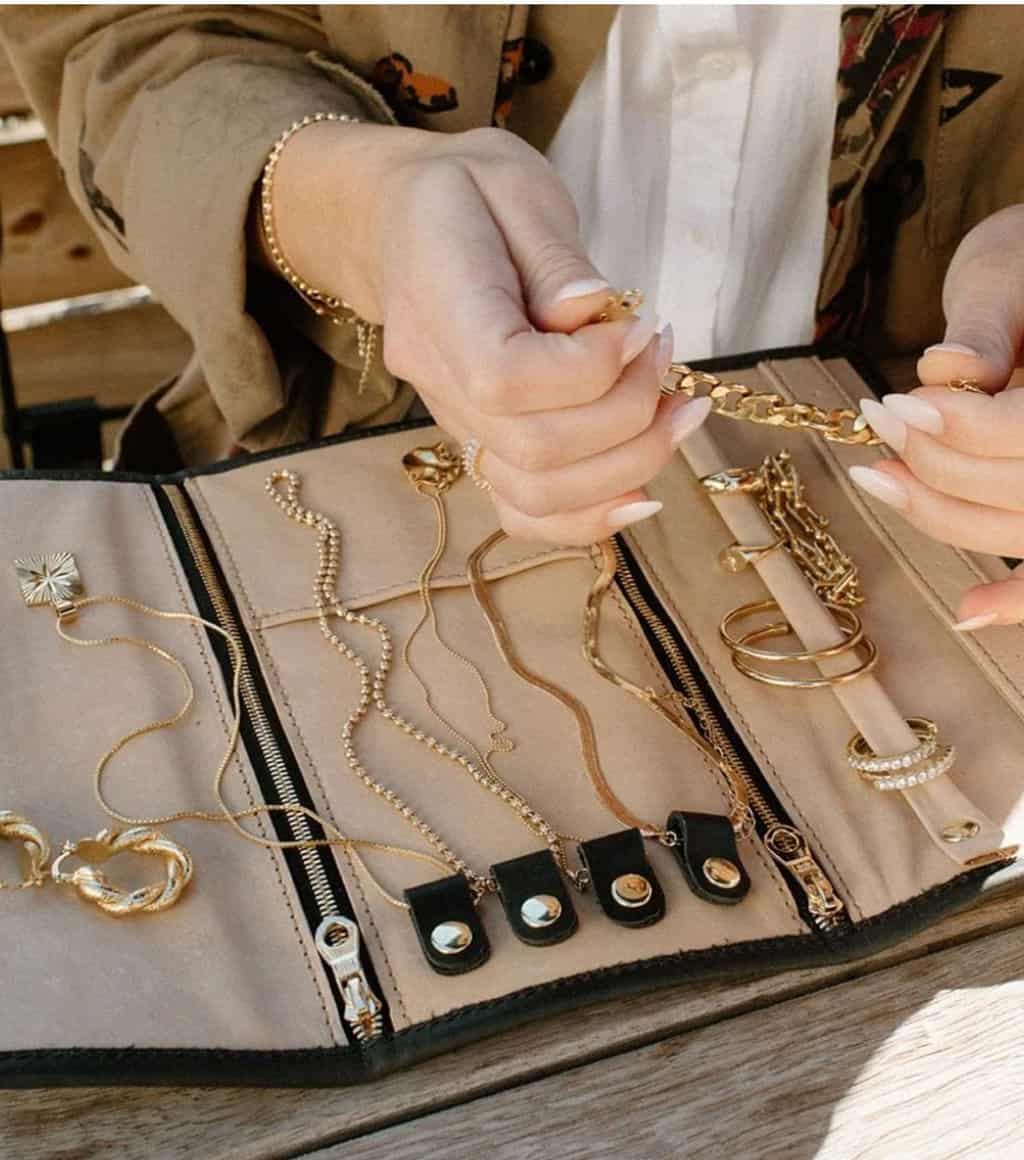 A womans manivured hands placing jewellery in a leather Jewellery wrap. 