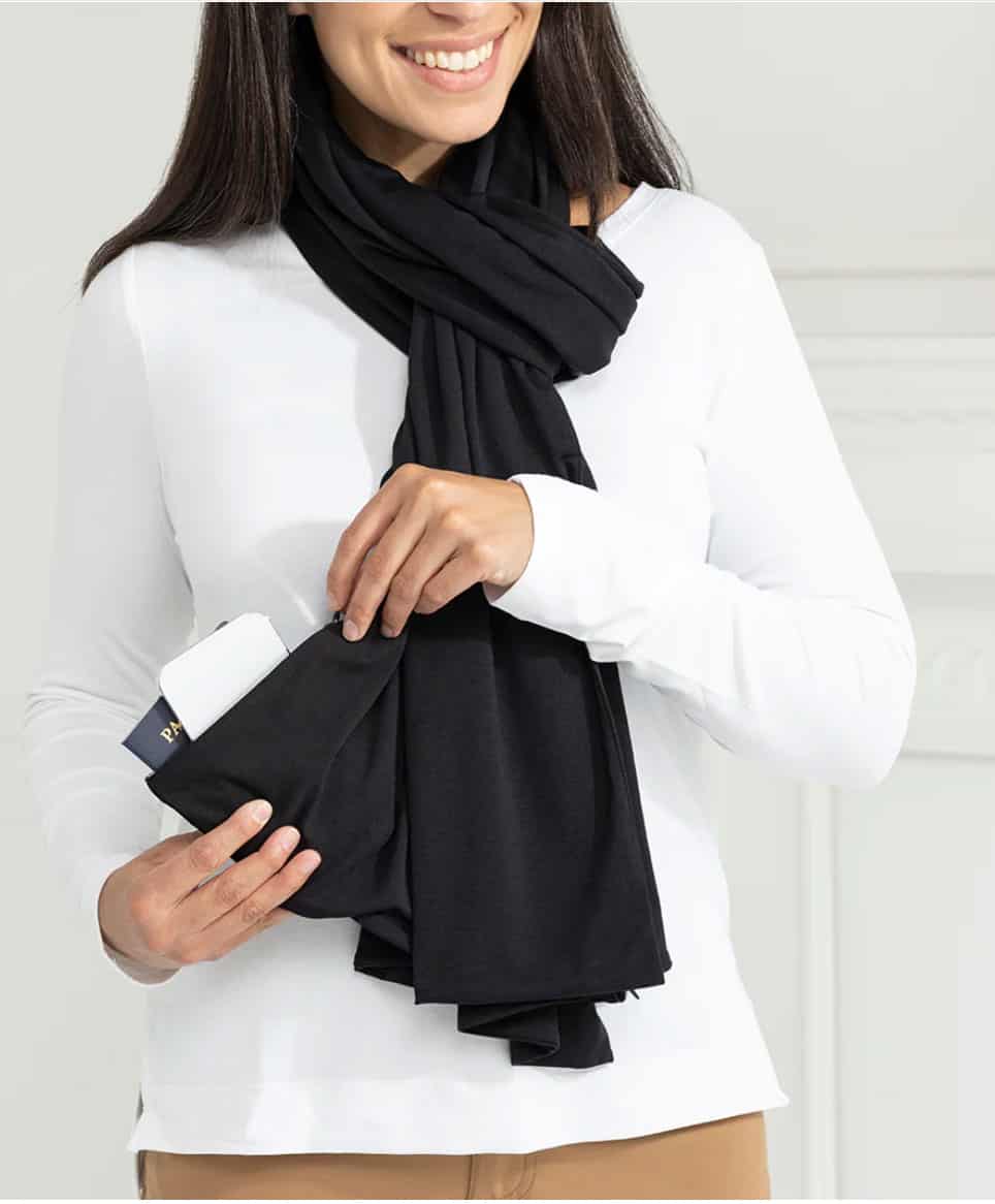 A woman in a white top modelling a black scarf with hidden pockets in the end.